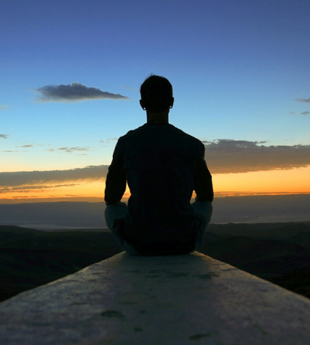 Person sitting cross legged in front of a sunset view