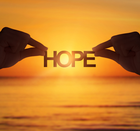 The word "HOPE" being held up in front of a sunset
