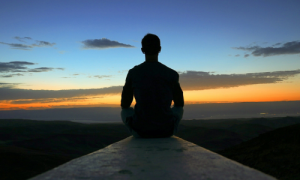 Person sitting cross legged in front of a sunset view