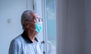 Senior with a mask on staring out the window