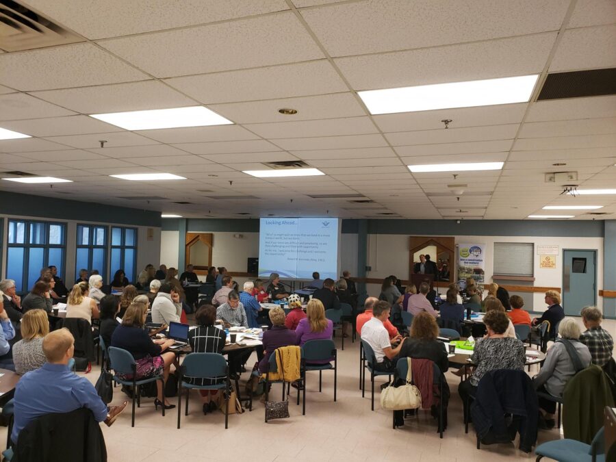 People sitting at grouped tables for a community forum watching a presentation