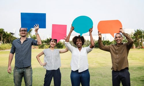 People holding different colour speech bubbles in a field